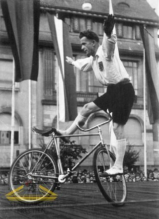 Das Foto zeigt einen Mann mit dunklen Haaren der auf einem Fahrrad balanciert vor den alten Frechener Rathaus.