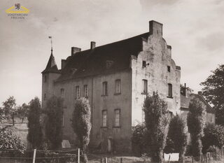 Schwarz-weißes Foto der Burg Benzelrath.Vor der Burg stehen schmale Bäume, am Zaun hängt Wäsche.