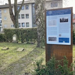 Infotafel mit Text und Bildern zu Gräbern von Zwangsarbeiterinnen und Zwangsarbeitern auf dem Bachemer Friedhof